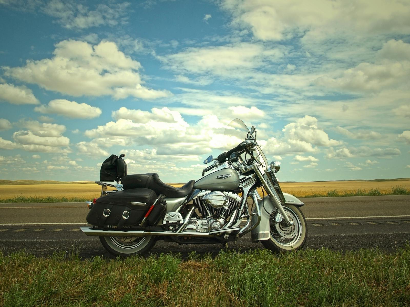 A lone motorcycle parked on an open road with a vast blue sky dotted with clouds for a sense of adventure.